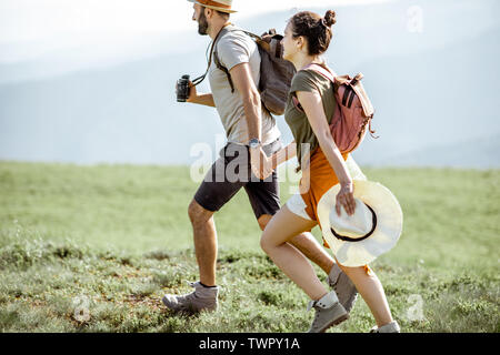 Bella giovane divertendosi, correndo insieme sul prato verde, mentre si è in viaggio in montagna durante il periodo estivo Foto Stock