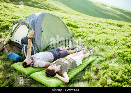 Giovane e allegro giovane sdraiato sul materasso al campeggio, godendo di estate durante un viaggio in montagna Foto Stock