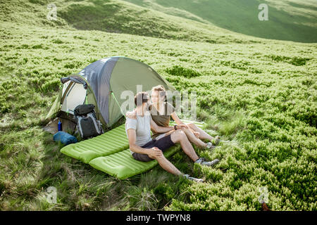 Giovane coppia adorabile seduti insieme sul materasso al campeggio, godendo di estate durante un viaggio in montagna Foto Stock
