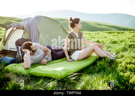 Giovane e allegro giovane sdraiato sul materasso al campeggio, godendo di estate durante un viaggio in montagna Foto Stock