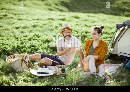 Giovane e allegro giovane avente un picnic presso il campeggio durante un viaggio in alta montagna durante il tramonto Foto Stock