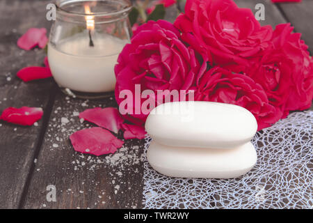 Cosmetici naturali sapone con rose rosse e candela a caldo sul legno scuro sfondo della spa Foto Stock