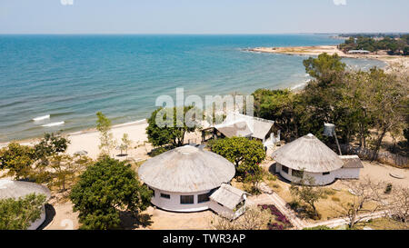 Vista aerea di un resort con chalet con tetto in paglia con il lago sullo sfondo in una giornata di sole Foto Stock