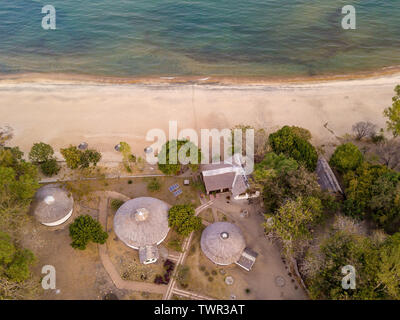 Vista aerea di un resort con chalet con tetto in paglia con il lago sullo sfondo in una giornata di sole Foto Stock