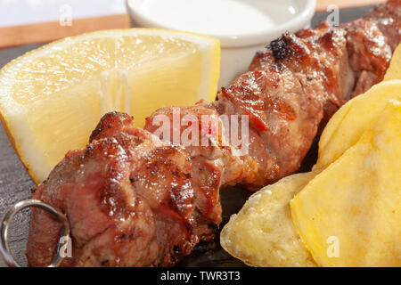 Tradizionale greco "'Souvlaki'' carne di maiale su un bastone di metallo servita con patatine fritte potatoe fette di limone e sulla piastra nera Foto Stock