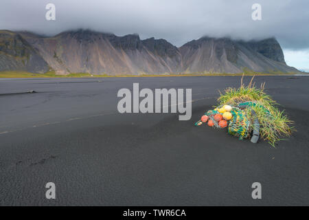 Vecchia rete da pesca scartato a qualche ciuffo di erba lungo la spiaggia di sabbia nera a Vestrahorn. Spiaggia inquinati con immondizia di plastica, immondizia di plastica. Foto Stock