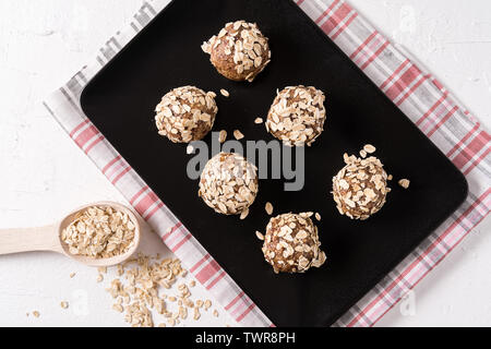 Sana energia organico palline fatte con date, fiocchi di avena, di mirtilli rossi secchi, noci pecan in piastra nera su sfondo bianco, piatto laici. Foto Stock