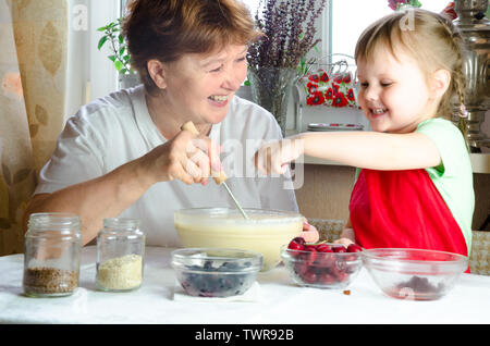 Ritratto di volti, mani felici i capelli castani granny, nipote. toddler girl gioca con la cottura, pasta di farina con cucina. bambino baby provare cookin studio Foto Stock