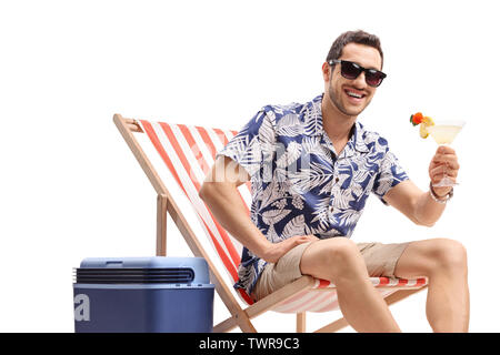 Giovane ragazzo con un cocktail seduti su una sedia a sdraio accanto a una scatola di raffreddamento e guardando la telecamera isolata su sfondo bianco Foto Stock