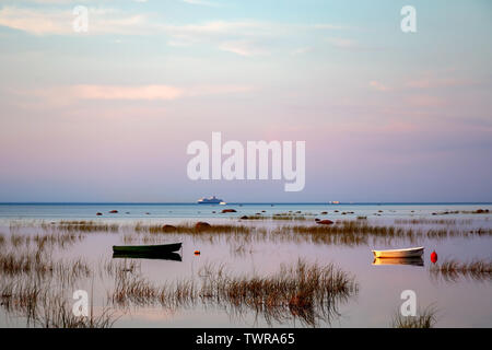 Le piccole imbarcazioni da pesca al di ancoraggio, che si riflette nelle calme e limpide acque del lago, sono coperti con sedge nelle prime ore del mattino contro la bellissima alba cielo di delicati toni pastello. Foto Stock