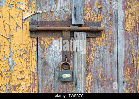 Il vecchio uomo delle salviette da un lucchetto sulla porta dell'edificio rurale. Protezione contro il deterioramento delle antiche porte. Stagione di estate. Foto Stock