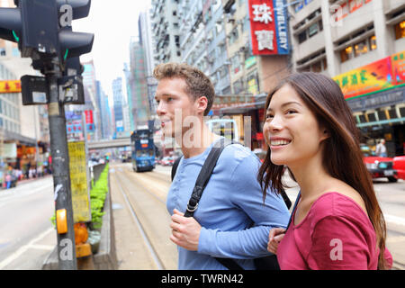 La gente di Hong Kong a piedi nella Baia di Causeway attraversamento strada trafficata con tram. Urban razza mista cinese Asiatica / Caucasian donna sorridente felice di vita in città. Foto Stock