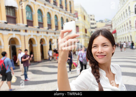 Donna turistica prendendo selfie foto a Macao Cina in Piazza Senado o Piazza del Senato. Ragazza asiatica tourist utilizzando smart phone fotocamera per scattare foto mentre sei in viaggio a Macao. Viaggi e turismo concept. Foto Stock