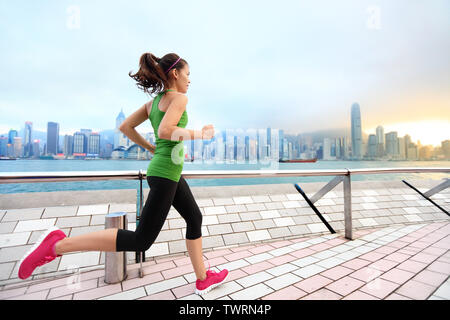 Città in esecuzione - donna runner e la skyline di Hong Kong. Atleta femminile atleta fitness training jogging vivere uno stile di vita sano in Tsim Sha Tsui Promenade e Avenue of Stars e nel Porto Victoria, Kowloon. Foto Stock