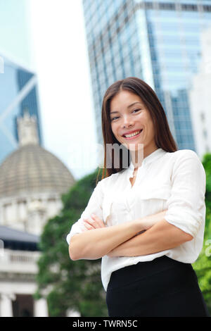 Business donna sorridente ritratto di Hong Kong. Imprenditrice piedi felici e di successo nel soddisfare cross-armato. Giovani e multirazziale asiatica Cinese / caucasico professionale femminile in centro a Hong Kong. Foto Stock