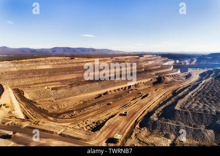 Deep exhavation di combustibili fossili minerali da taglio aperto nero miniera di carbone nella Hunter Valley bacino di carbone di Australia con macchine industriali, camion e e Foto Stock