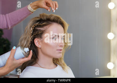 Parrucchiere trecce di tessitura in un salone di bellezza. Servizi di parrucchiere. Сreating acconciatura. Procedimento dell'acconciatura dei capelli. Parrucchiere utilizza spray-conformato la lacca Foto Stock