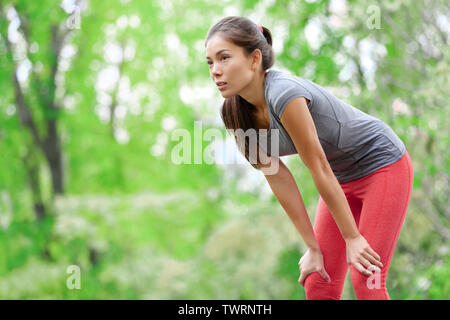 Donna asiatica atleta runner riposo dopo la corsa e il jogging all'aperto di formazione nella foresta. Stanco esaurito bellissimo sport modello fitness vivere sano stile di vita attivo. Razza mista Asian caucasiche. Foto Stock