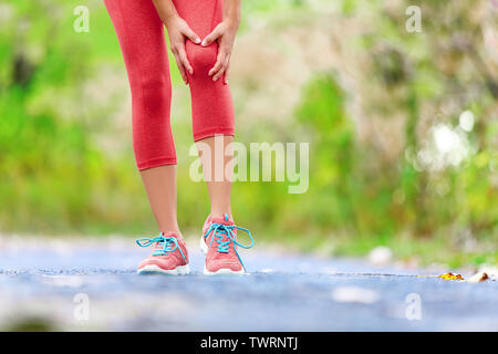 Infortunio al ginocchio - sport in funzione delle lesioni al ginocchio sulla donna. Guida femmina con dolore dalla distorsione del ginocchio. Close up di gambe, il muscolo e il ginocchio all'aperto nella foresta. Foto Stock