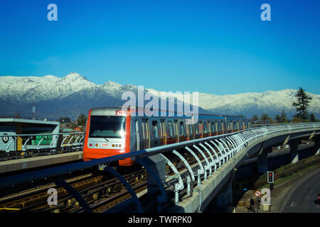 SANTIAGO DEL CILE - Giugno 2014: un acciaio Santiago treno Metro entrando in stazione di Trinidad, con le montagne innevate sullo sfondo Foto Stock