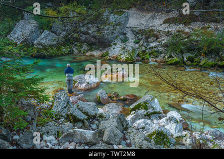 Pescatore solitario la pesca di trote lungo il fiume Soca in Slovenia. La pesca con la mosca in waders per la pesca alla trota lungo immacolate fiume di montagna con rapide. Foto Stock