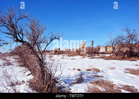 Crimea coquina blocchi di roccia rovinato farm pareti due torri d'acqua, asciutto erba spiovente campo coperto di neve, cespugli di bacche di sambuco senza foglie crescente Foto Stock