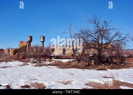 Crimea coquina blocchi di roccia rovinato farm pareti due torri d'acqua, asciutto erba spiovente campo coperto di neve, cespugli di bacche di sambuco senza foglie crescente Foto Stock