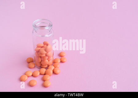 Le compresse di colore arancione dalla bottiglia di vetro su sfondo rosa. copyspace per il testo. Epidemia, antidolorifici, healthcare, trattamento pillole e abuso di droga concetto. Foto Stock