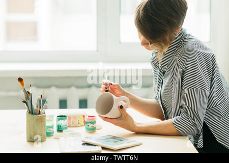 La ceramica donna tiene in mano una tazza di dipingere l'ornamento, di ceramica fatti a mano Foto Stock