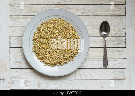 È germogliato il grano saraceno in piastra bianca e cucchiaio bianco su un tavolo di legno. Vista dall'alto. Posizione centrale. Concetto di alimentazione sana. Cibo vegan. Materie organiche hu Foto Stock