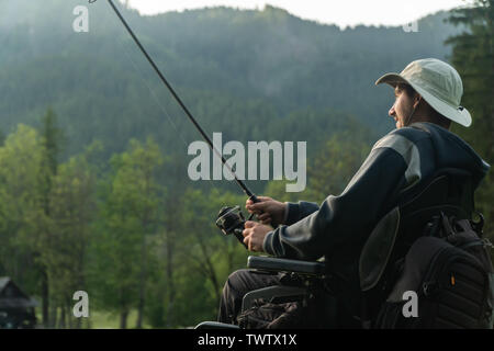 Giovane uomo su una sedia a rotelle la pesca al bel lago tramonto, alba Foto Stock