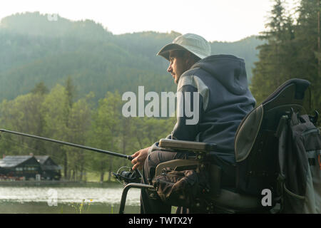 Giovane uomo su una sedia a rotelle la pesca al bel lago tramonto, alba Foto Stock