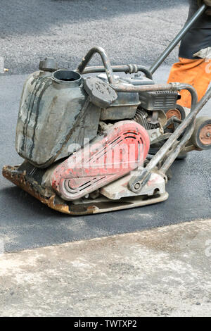 I lavoratori stradali compact l'asfalto con una vibrante rammer sulla strada. Lavoratore con compattatore a una strada in costruzione sito. foto verticale. Foto Stock