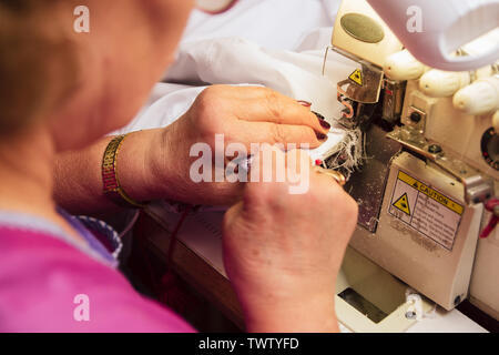 Una donna anziana cuce su una macchina da cucire sarto ricama in produzione. pensionato impegnato hobby preferito. Foto Stock