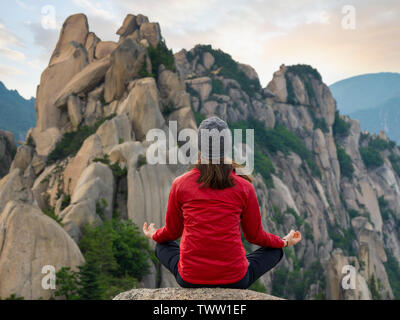 Con le gambe incrociate giovani escursionista meditando sulla sommità del monte Ulsan in Corea del Sud durante il tramonto Foto Stock