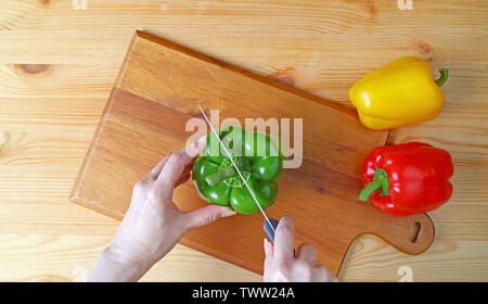 Donna di taglio a mano un peperone verde sul tagliere di legno Foto Stock