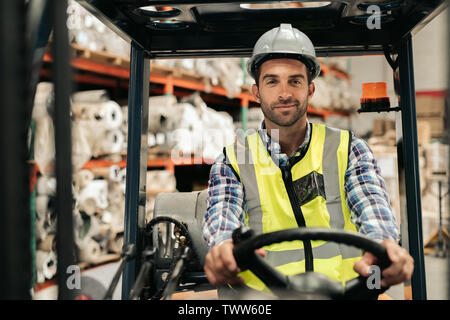 Sorridente driver di carrelli elevatori in movimento su stock a magazzino Foto Stock