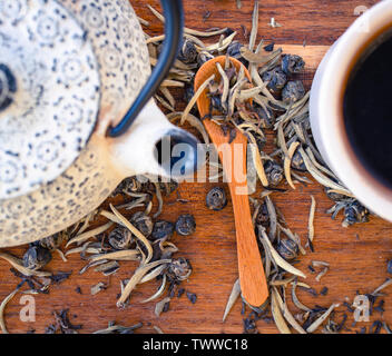 Una chiusura della teiera e tazza di tè rosso, tè verde e tè bianco lascia su di un tavolo di legno Foto Stock