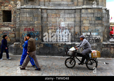 Uomo di consegna sulla bicicletta passato rivoluzionario e graffiti ritratto di John Lennon sulla parete laterale della Cattedrale Primaziale, Bogotà, Colombia Foto Stock