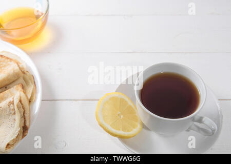 Tè nero in una tazza bianca con frittelle e miele su uno sfondo luminoso Foto Stock