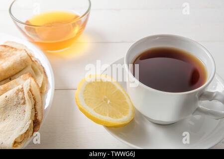 Tè nero in una tazza bianca con frittelle e miele su uno sfondo luminoso Foto Stock