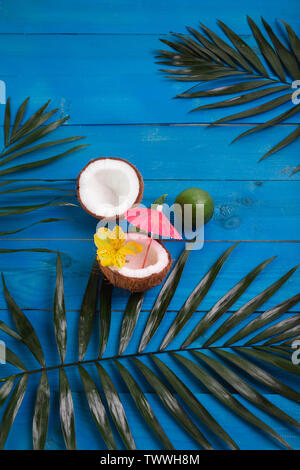 Noci di cocco, lime e foglie di palmo in blu sullo sfondo di legno. Appartamento laico, spazio per il testo Foto Stock
