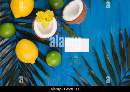 Limone, calce, noce di cocco e foglie di palma e business card su blu sullo sfondo di legno. Foto Stock