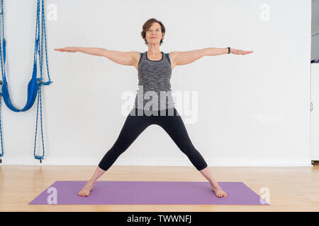 Un vecchio di 70 anni donna istruttore yoga nel suo studio mostra posizione Yoga chiamato Virabhadra posa è anche conosciuto come il guerriero pongono Foto Stock