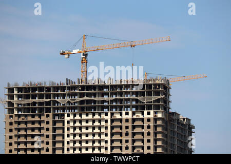 Gru edili e gli edifici residenziali in costruzione sullo sfondo del cielo blu con nuvole bianche Foto Stock