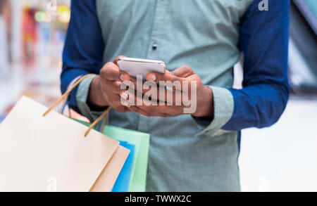 Irriconoscibile ragazzo africano con borse per lo shopping tramite cellulare Foto Stock