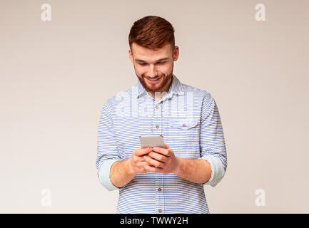 Giovane uomo absorbedly la messaggistica di testo sul suo cellulare Foto Stock