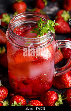 Close up strawberry limonata con ghiaccio in vaso con bacche e foglie di basilico Circa su sfondo scuro. Foto Stock