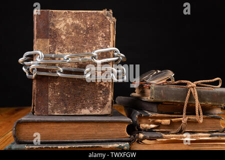 Un vecchio libro legato da un metallo lucido catena. Vietato letteratura disposti su di un tavolo di legno. Sfondo scuro. Foto Stock