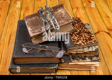 Un vecchio libro legato da un metallo lucido catena. Vietato letteratura disposti su di un tavolo di legno. Sfondo scuro. Foto Stock